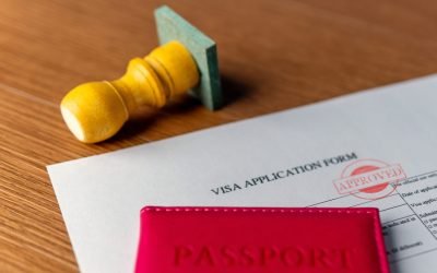 A visa application form with "APPROVED" stamp, a red passport, and a rubber stamp. International travel, permit, official consent concept.